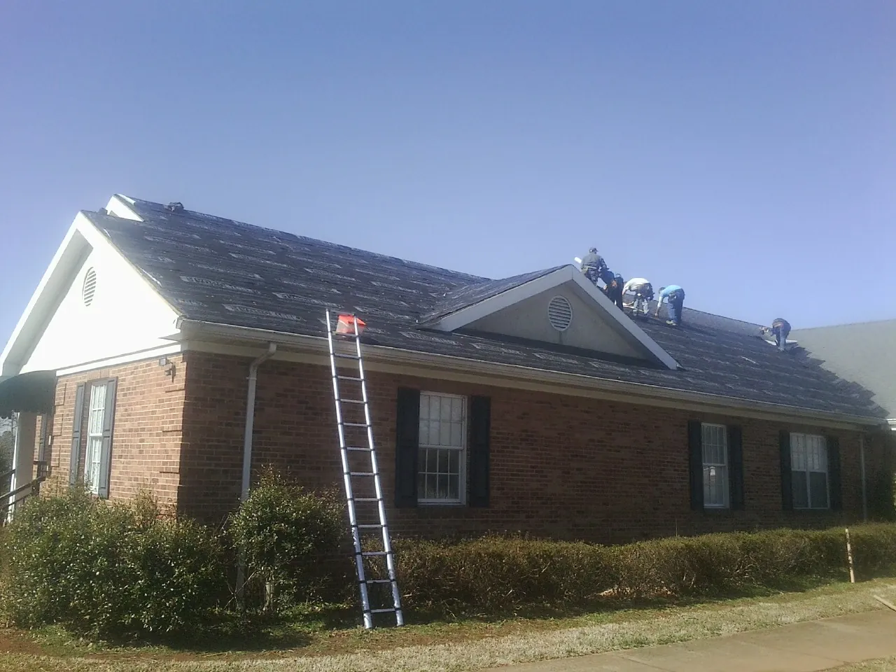 Crew tearing shingles off a brick ranch roof with a ladder set — Emergency Roof Repair work by our crew in Harwich Port