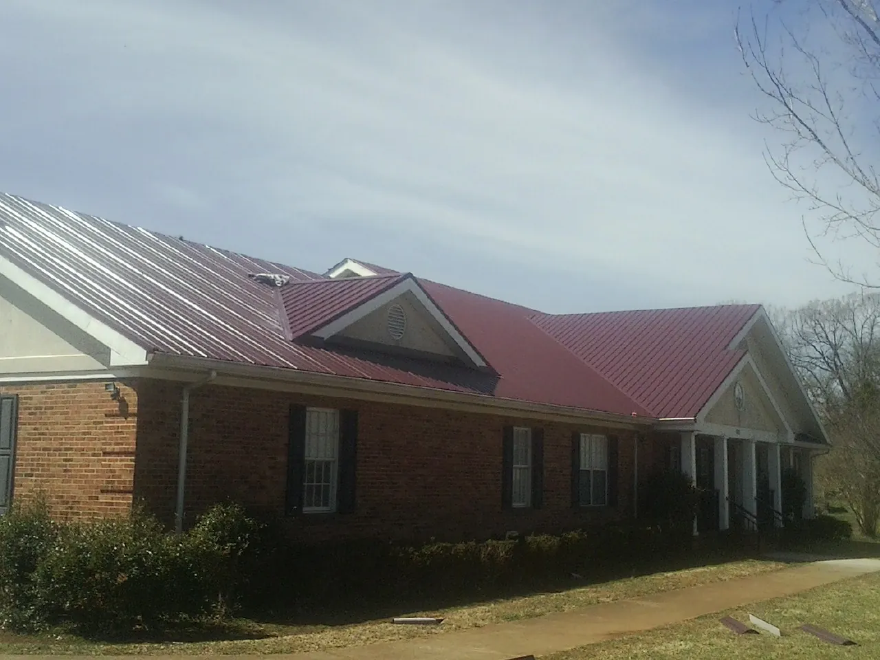 Red metal roof with gabled entries on a long brick building, from a Hail Damage Roof Repair job in Harwich Port