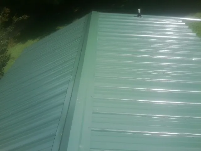 New green metal panels meeting at the ridge of a roof — Flat Roof Repair work by our crew in Harwich Port