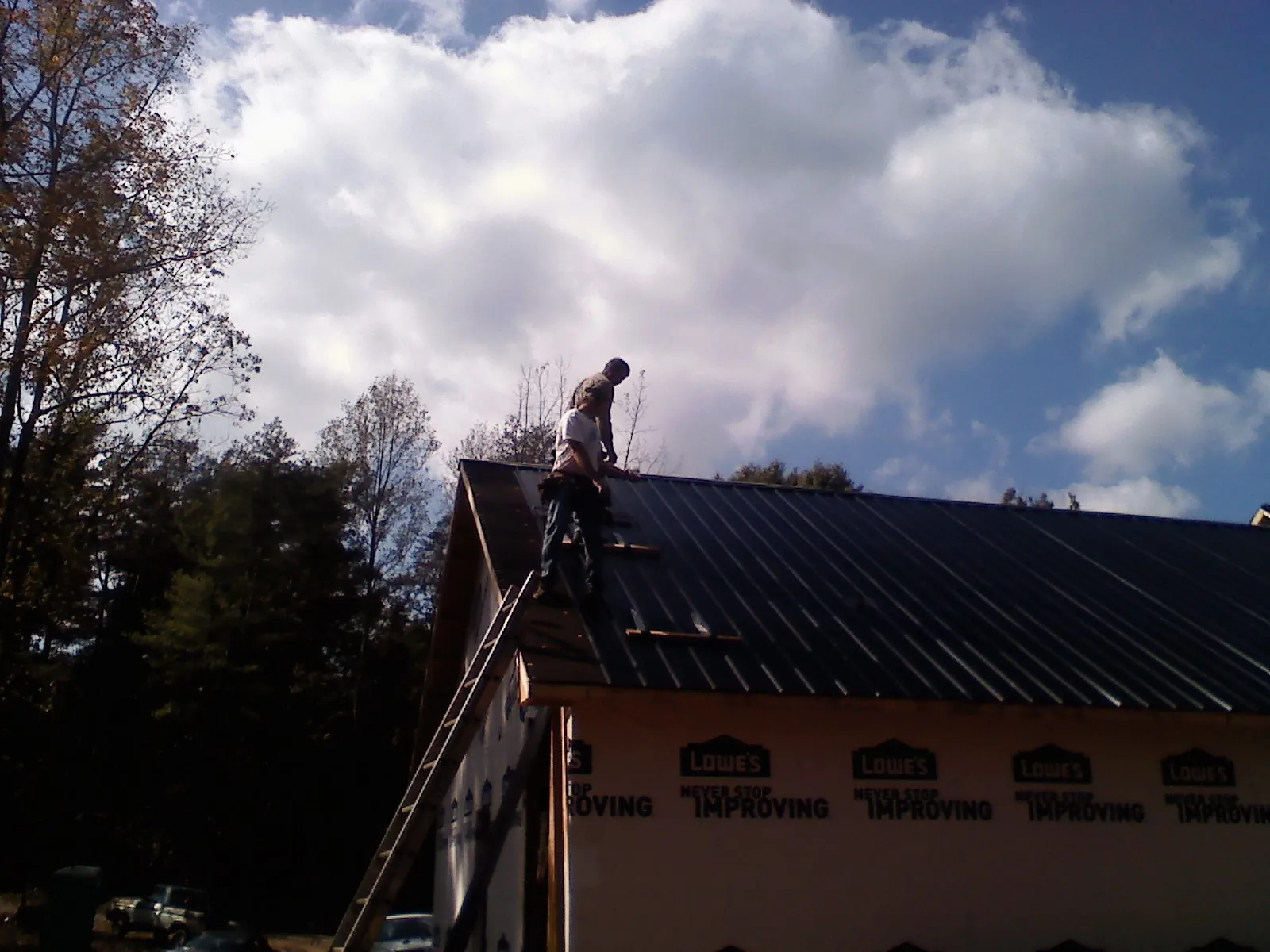 Roofer fastening dark metal panels high against a cloudy sky, from a Roof Inspection job in Harwich Port
