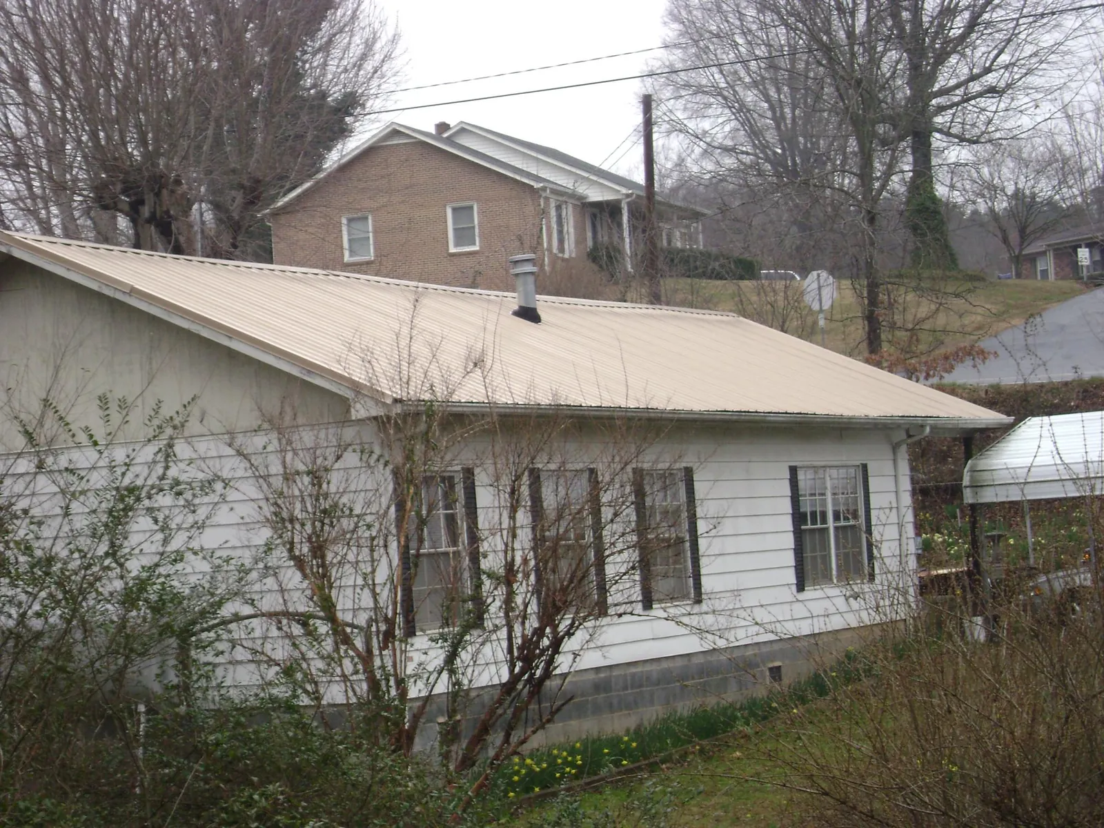 Tan metal roof on a white sided house set into a hillside — Commercial Roofing by Roofing Brothers in Harwich Port